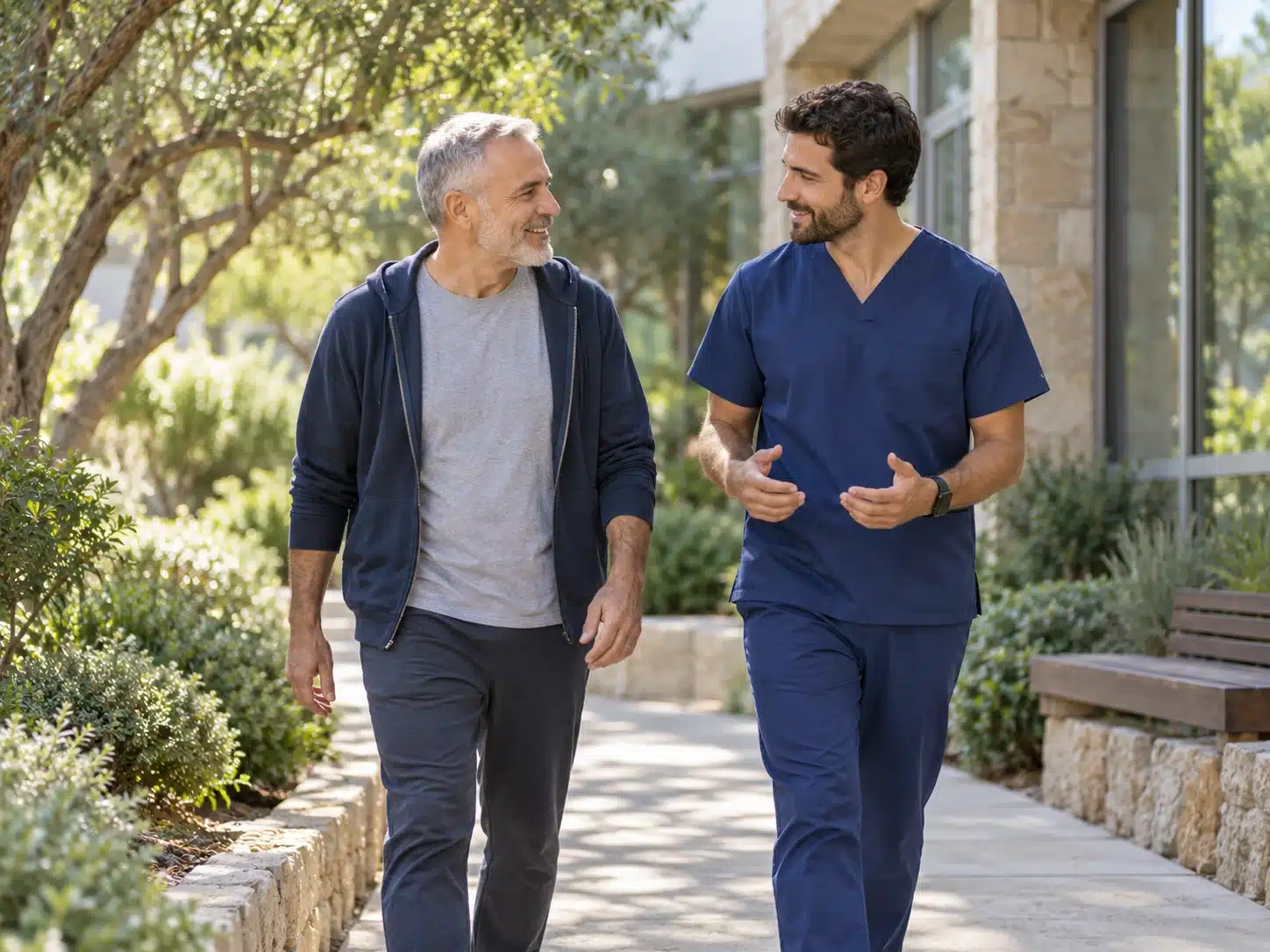 גבר אחרי תקופת טיפול הולך בקצב רגוע עם מטפל בשביל קצר ומוצל סמוך למרפאה